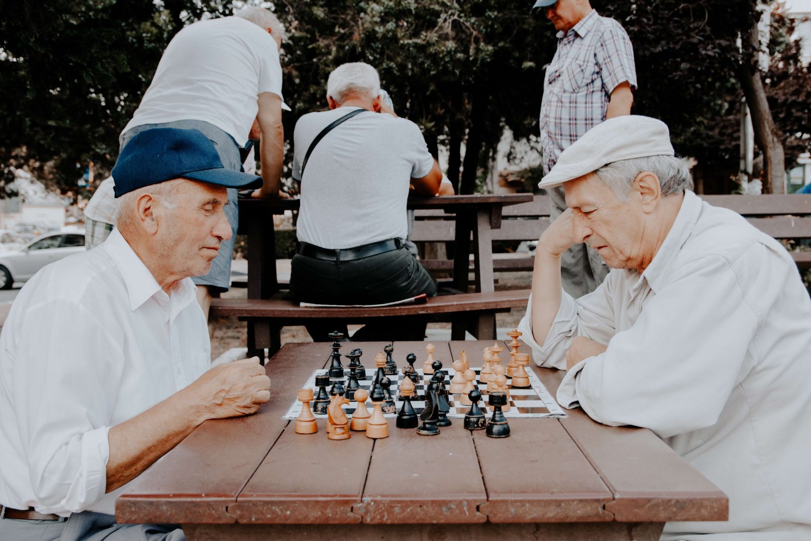 Two older men playing chess in a park at a picnic bench