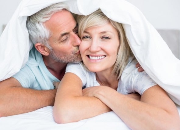 Elderly couple smiling under a duvet.