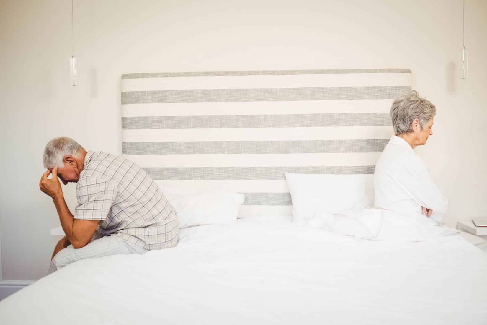 upset senior couple sitting on the opposite ends of the bed after a fight about what causes erectile dysfunction