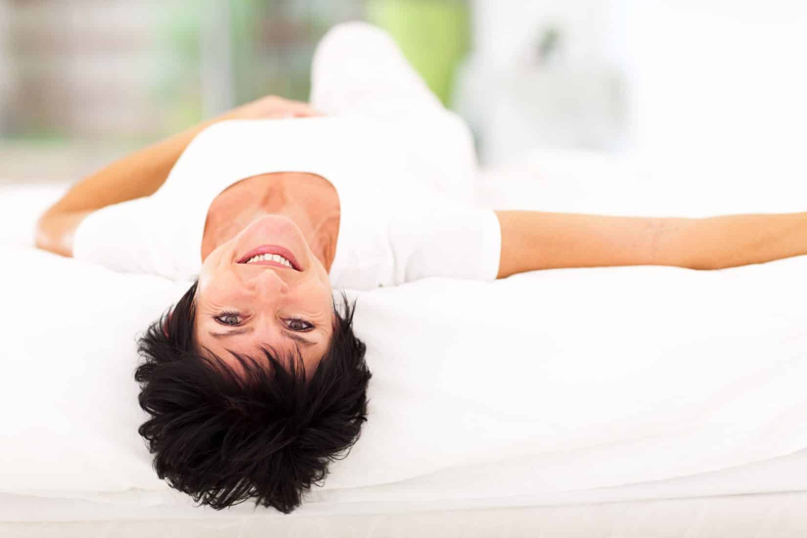 middle-aged woman laying on bed and smiling at camera