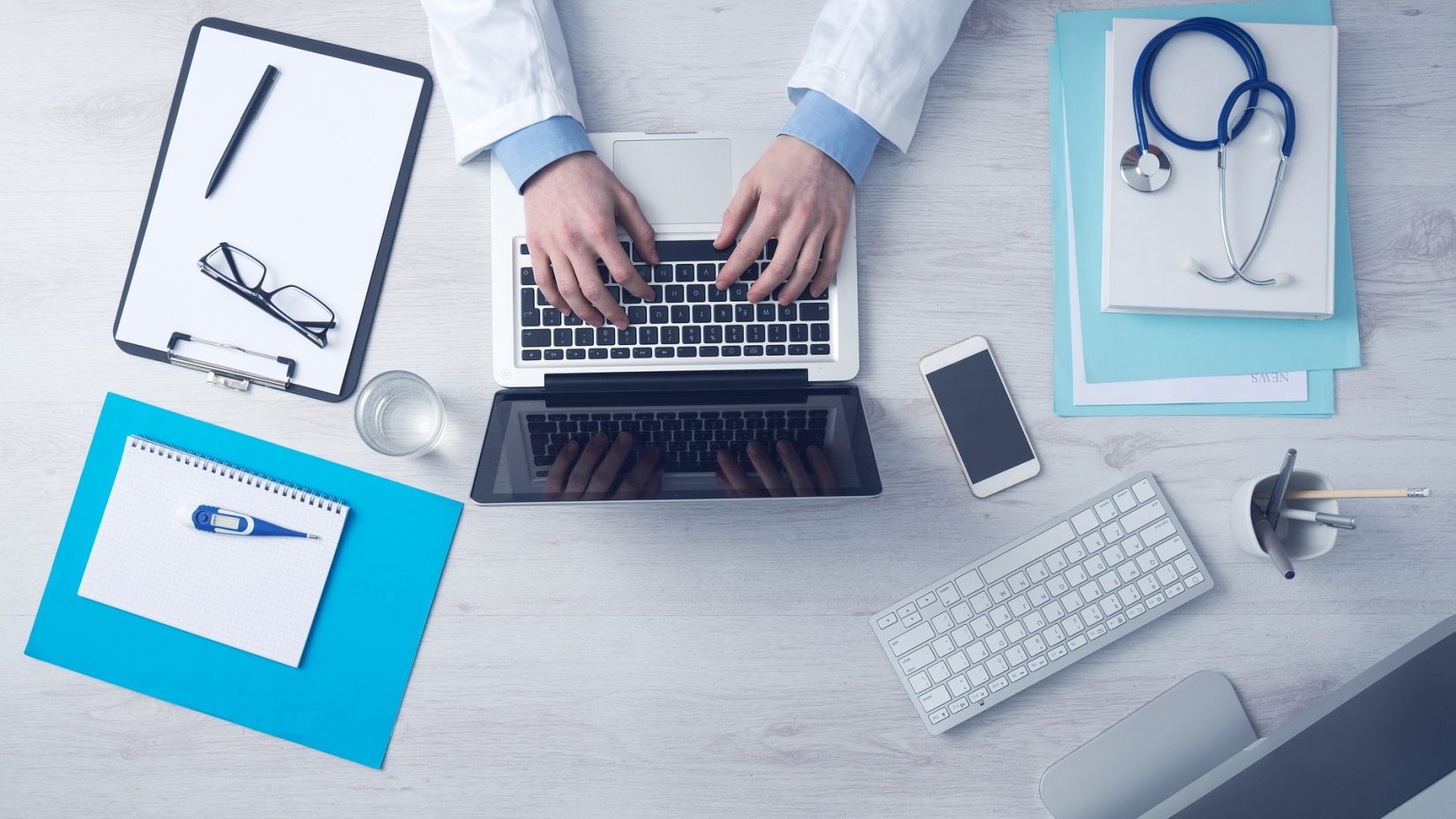 Doctor Typing on Laptop with Paperwork on Desk