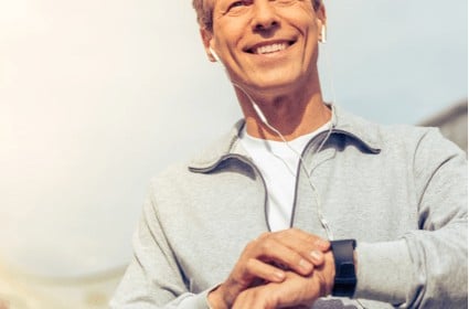 White man outdoors holding watch and using earbuds