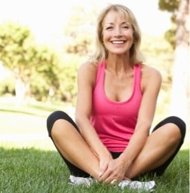 Smiling white woman sitting in gym clothes outside on the grass