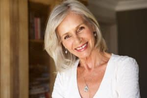 Older woman with white shirt on smiling while tilting her head to the side