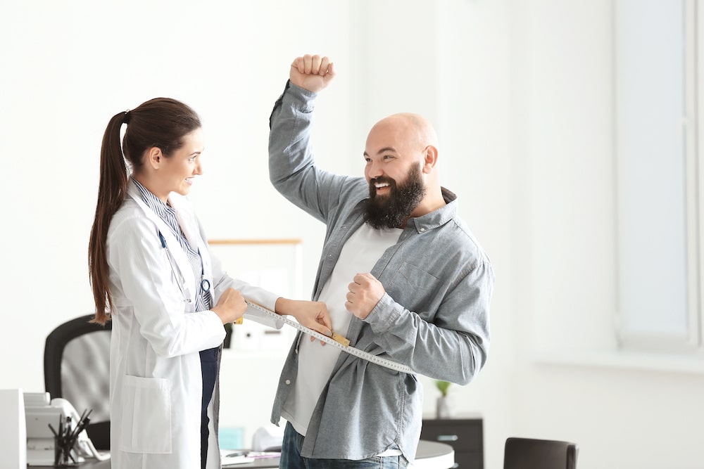 Young female doctor measuring waist of overweight man in clinic