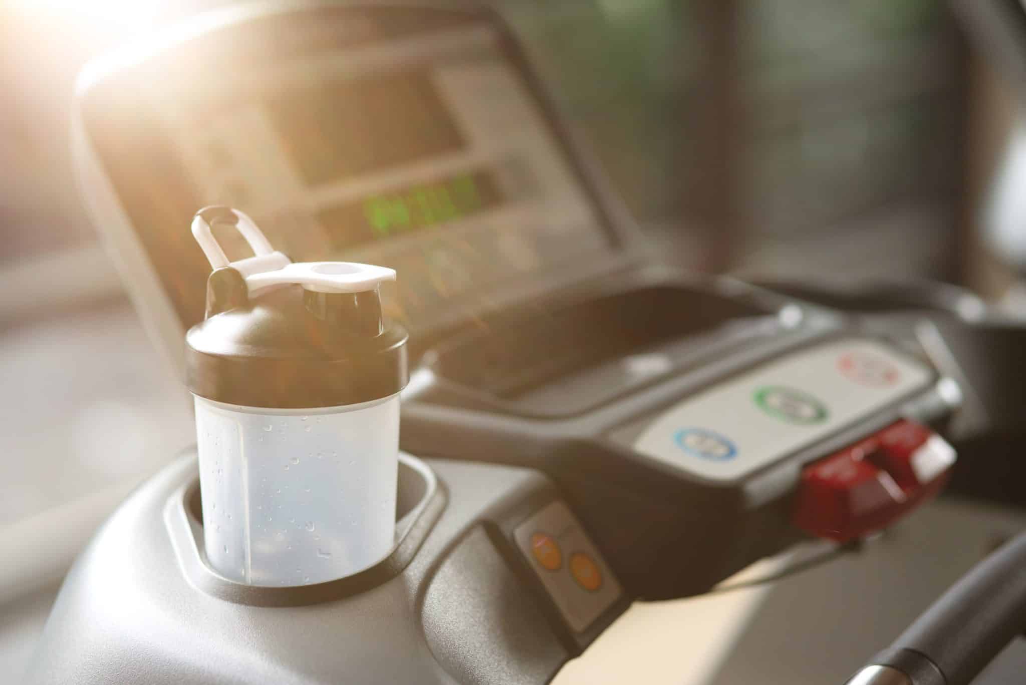 A treadmill with a shaker bottle in the cup holder.