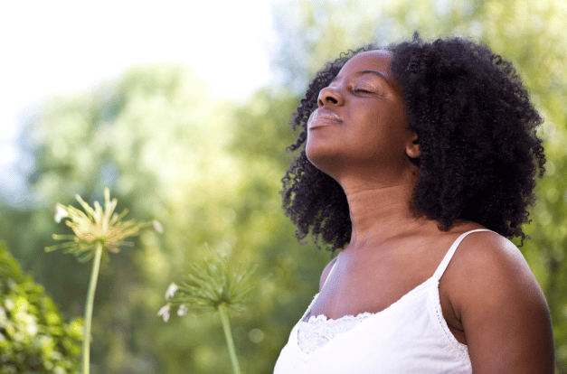 Girl with their eyes closed basking in the sun surrounded by plants.