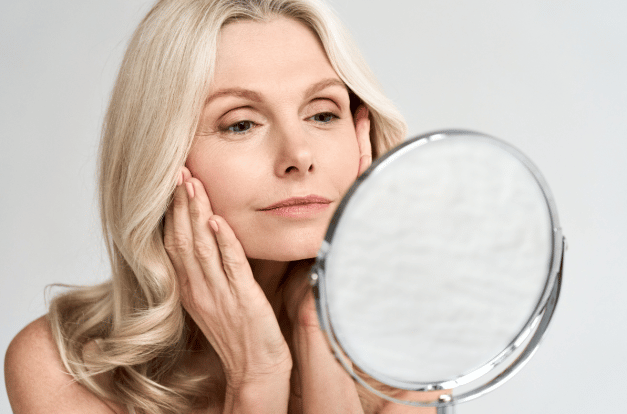 Mature women holding their face looking at a mirror.
