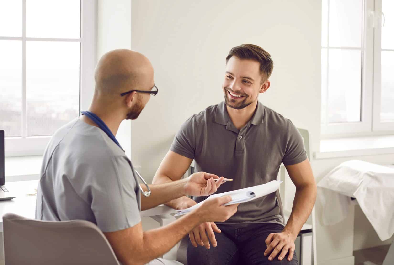 A healthcare professional in scrubs consults with a smiling patient in a clinic.