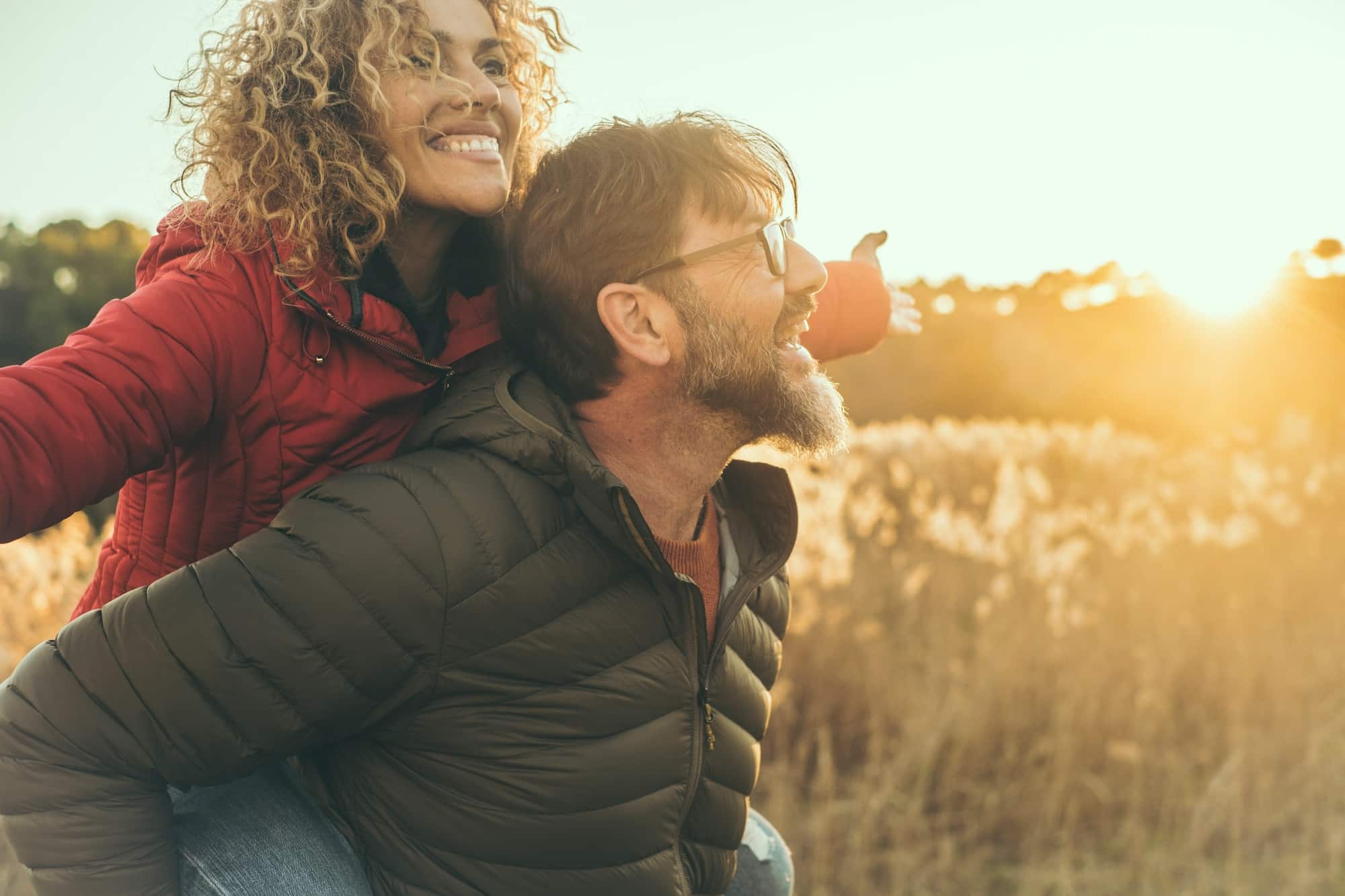 Smiling couple in a field with the man carrying the woman on his back