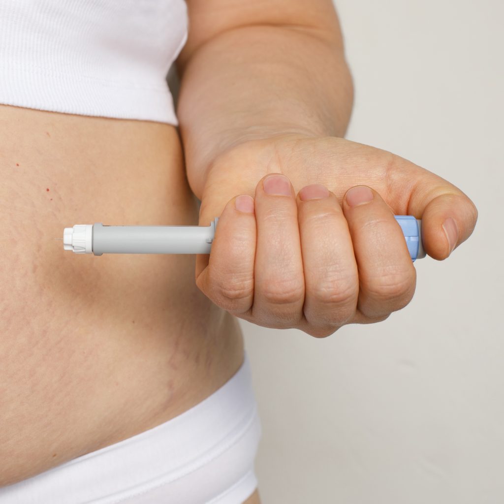 A person's abdomen with a gray and blue Ozempic pen injecting semaglutide.