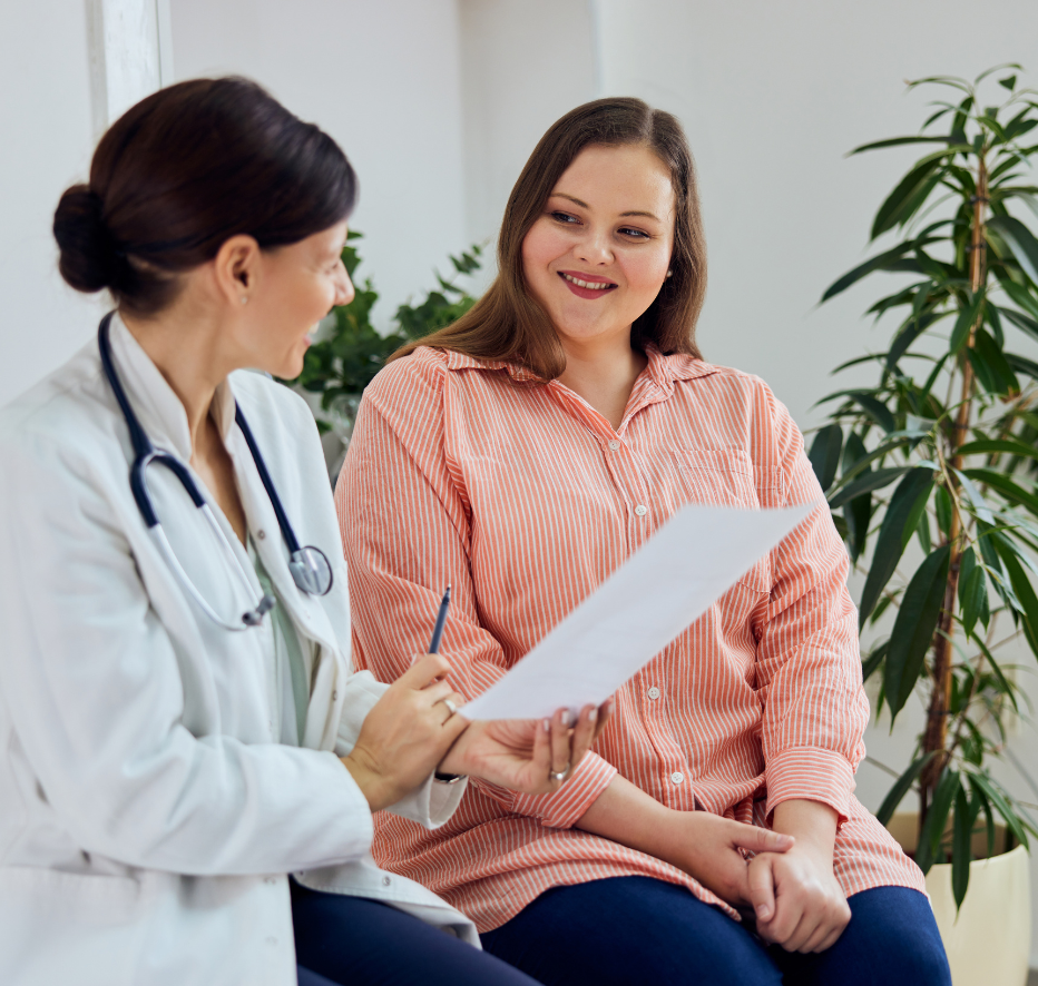 A weight loss doctor in a white coat with a stethoscope discussing a document with a smiling patient in a striped shirt, seated in a clinic.