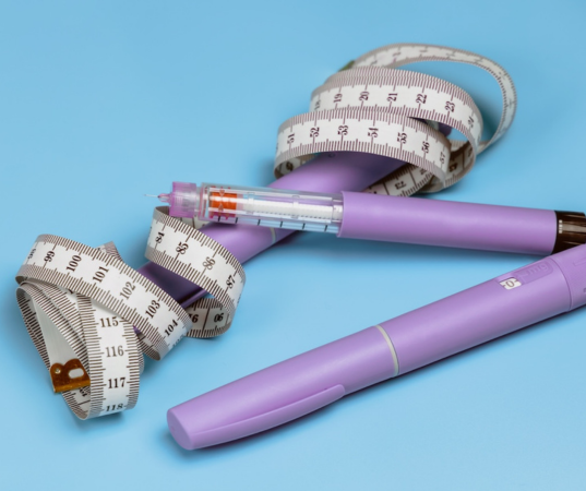 A purple GLP-1 agonist pen next to a coiled measuring tape on a blue background.