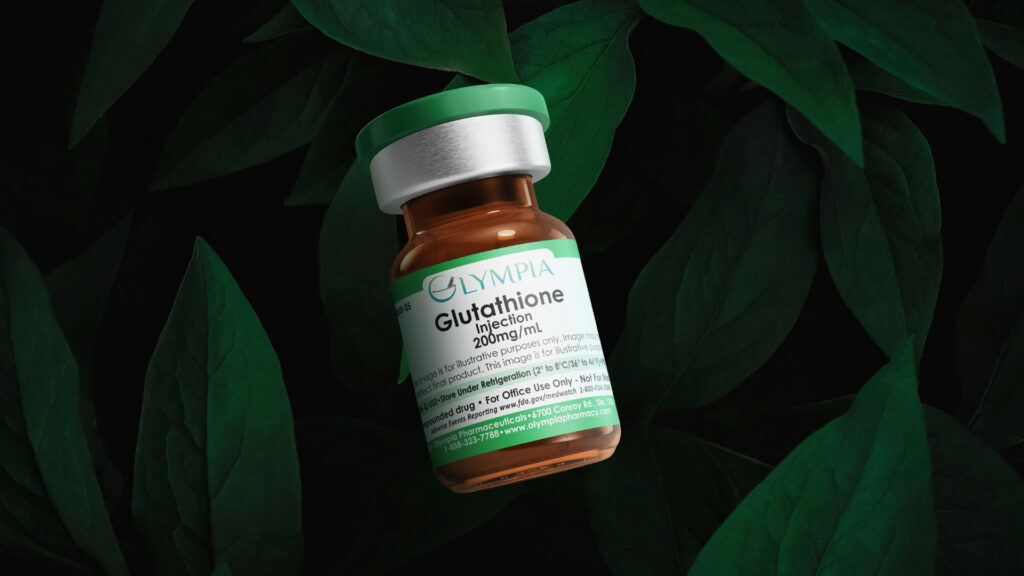 A vial of injectable Glutathione hovers in front of a dark background surrounded by leaves. The vial is amber, has a green cap and label, and reads "Olympia Glutathione Injection 200mg/mL."