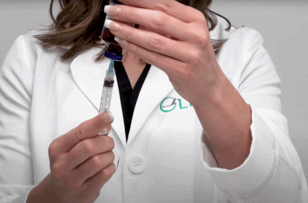 A video thumbnail demonstrating an intramuscular injection. A pharmacist can be seen drawing medication from a sterile vial of MICC.