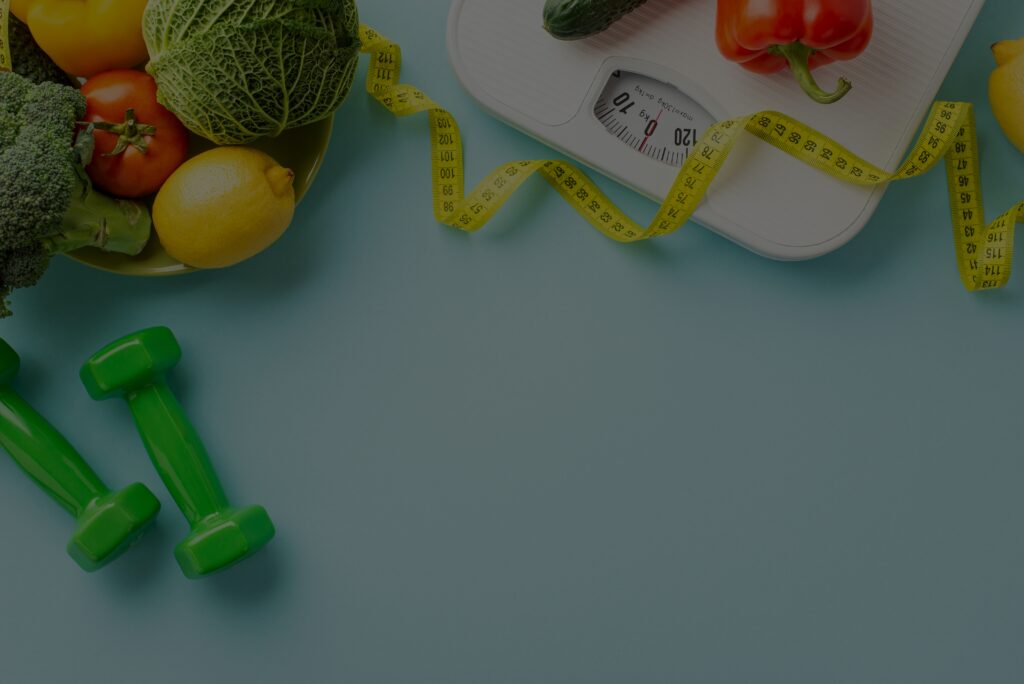 Flat lay of healthy lifestyle items including fresh vegetables, a lemon, green dumbbells, a white bathroom scale and a yellow measuring tape on a blue background.