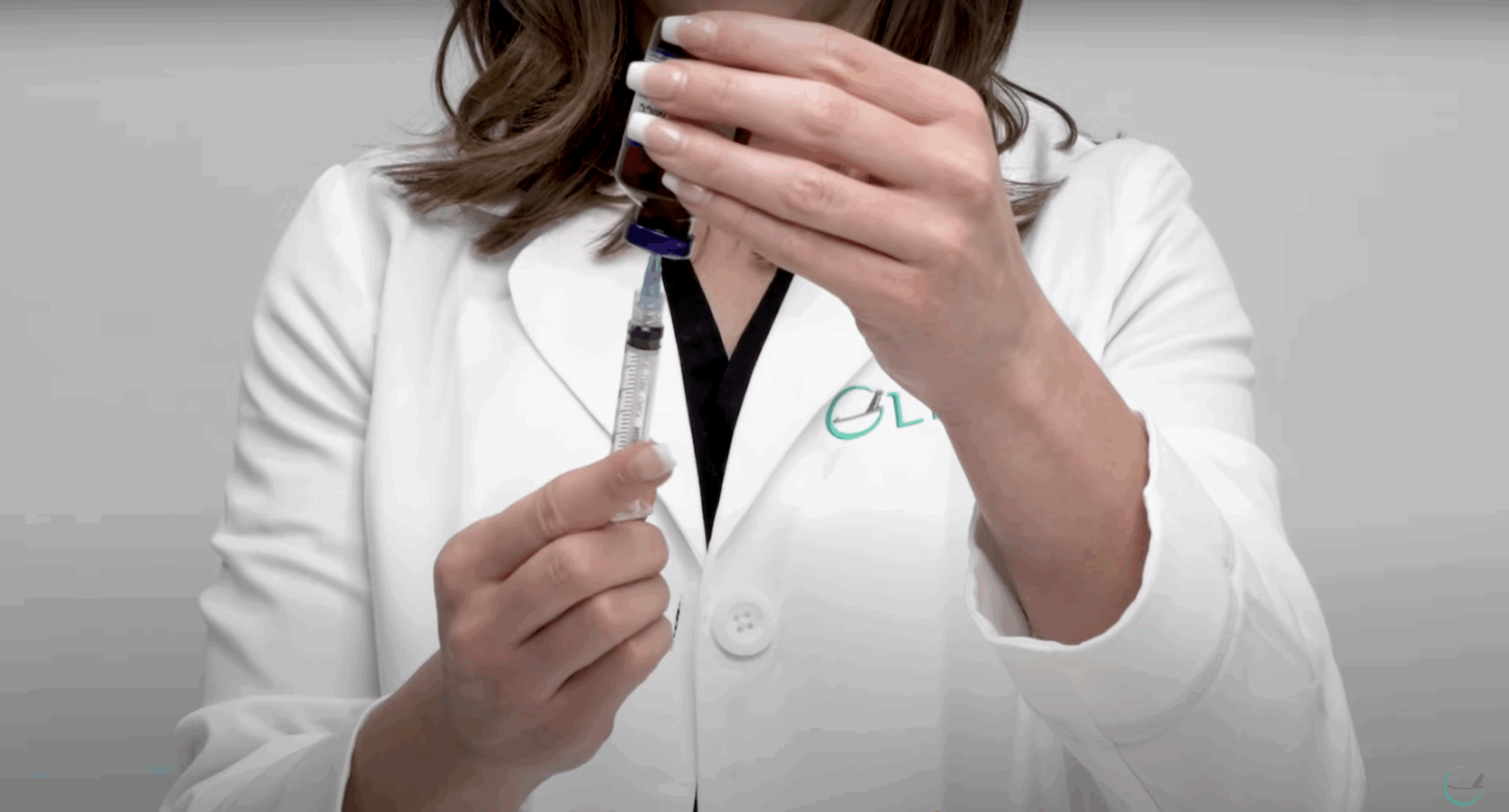 Healthcare professional drawing medication from an inverted vial into a syringe while wearing a white lab coat.