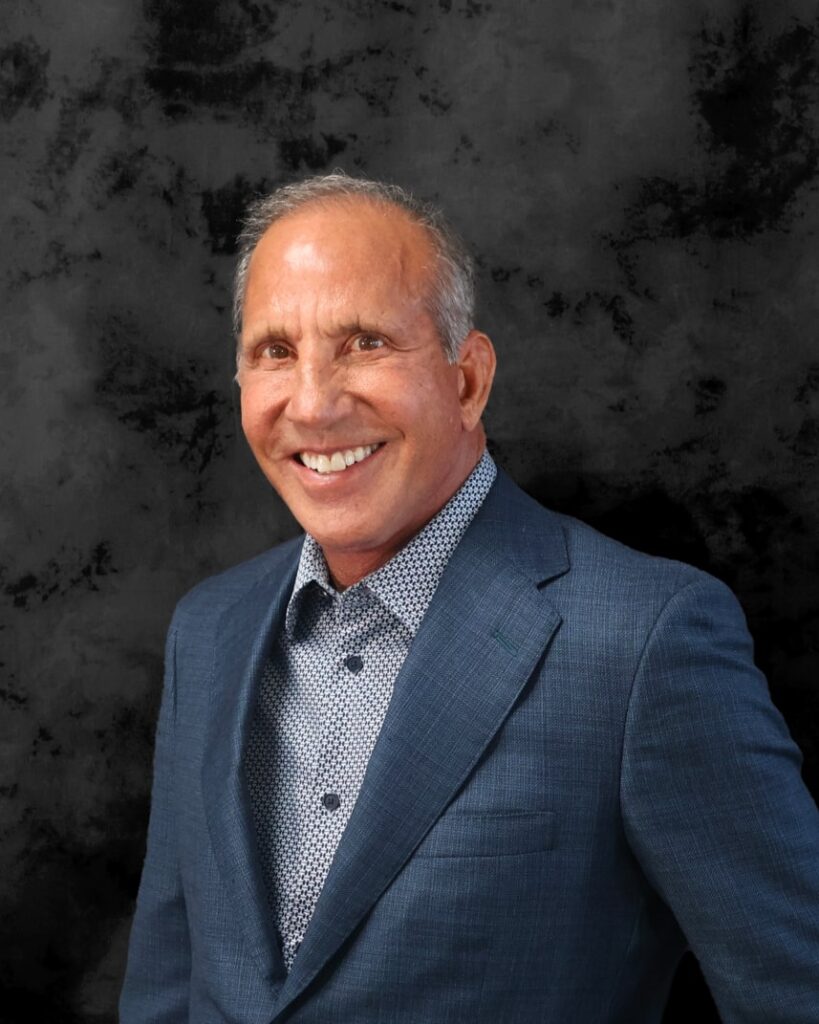A professionally shot headshot of Stan Loomis, co-founder of Olympia Pharmaceuticals. Stan is seen wearing a dark gray-blue suit and gray dress shirt.