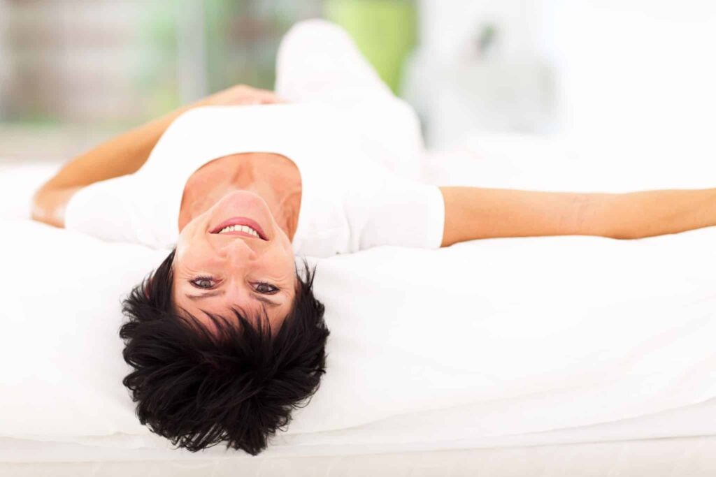 Middle-aged woman laying on bed and smiling.
