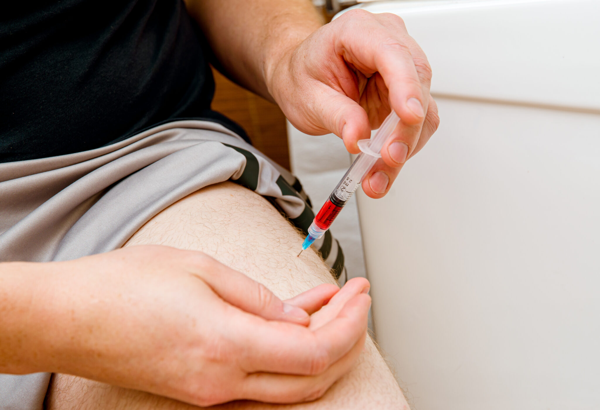 A man administers an intramuscular injection into his thigh using a syringe.