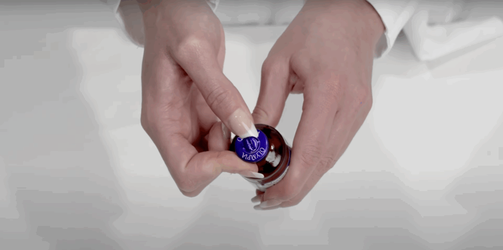 Close-up of hands removing the foil seal from the top of a medication vial labeled Olympia.